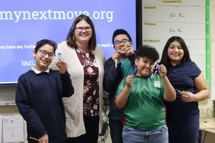 Four middle school students smiling with their teacher in a classroom
