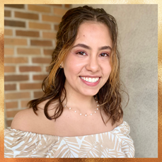 Deni, a young college student, is standing in front of a brick wall, smiling into the camera.