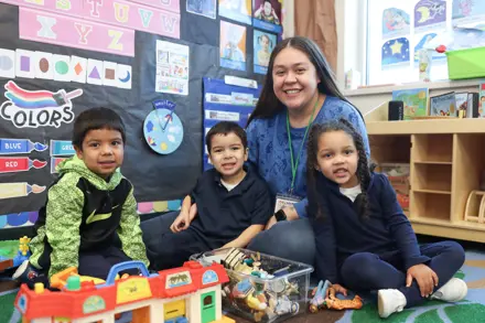 Photo of female teacher sitting on the classroom rug with her young students smiling