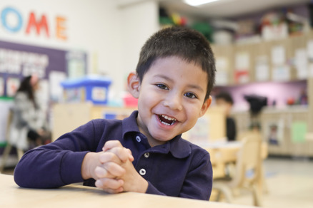 UCC Kindergarten Student Santiago smiling at his desk in a classroom