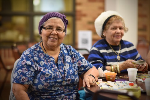 Photo of two female Senior Center clients sitting at a table at the senior center playing a game and smiling