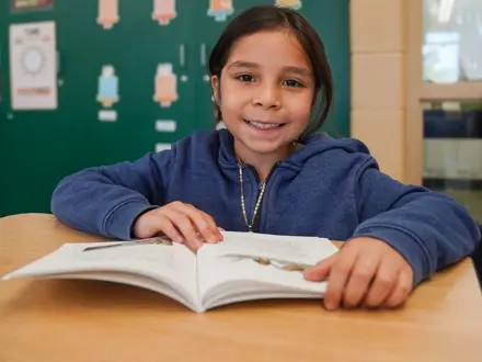 Middle school girl reading a book at her desk and smiling