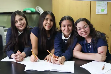 Four Middle School Students in a classroom working on an assignment and smiling